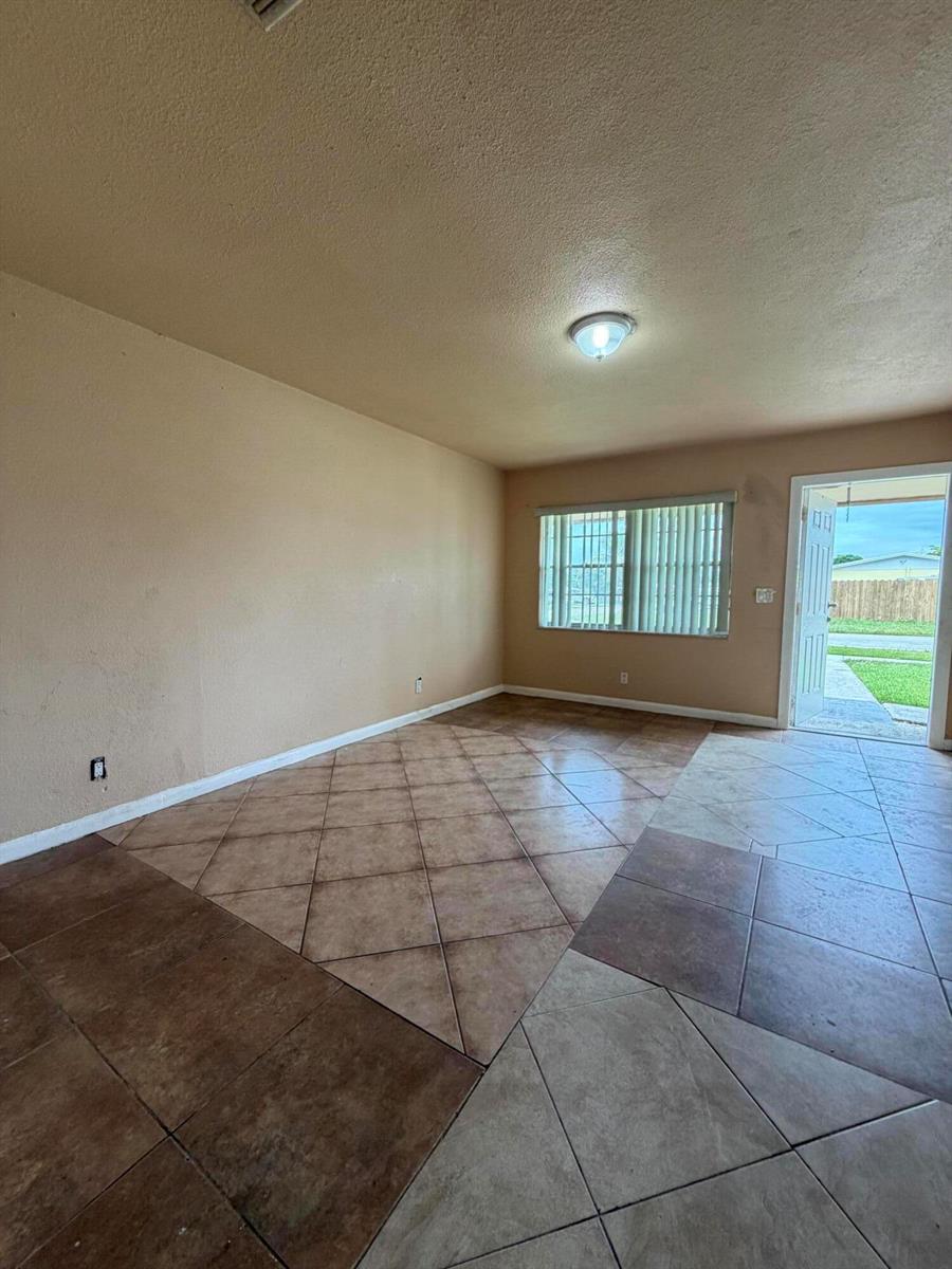 An empty room features tan walls, a light fixture, and diagonal brown tile flooring — 3243 Grove Road, Boynton Beach FL 33435, BOYNTON BEACH, FL