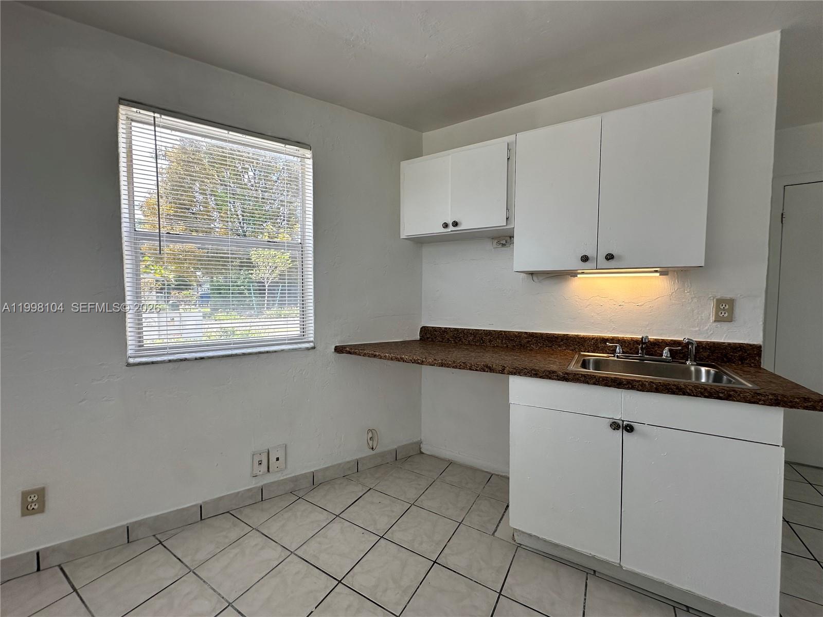 A kitchen features white cabinets, a brown speckled countertop, a sink, and tiled flooring — 701 NW 7th Ave # 1, Hallandale Beach FL 33009, HALLANDALE BEACH, FL
