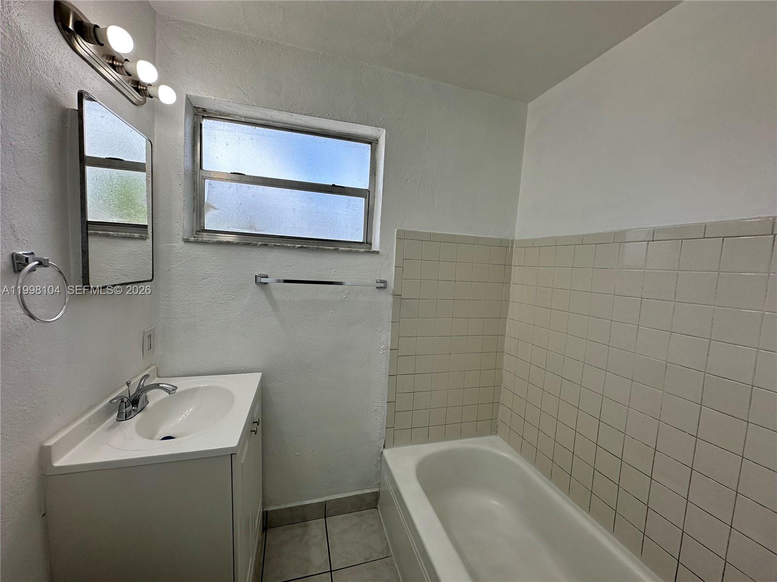 A bathroom features a white vanity, a bathtub with beige wall tiles, and a window — 701 NW 7th Ave # 1, Hallandale Beach FL 33009, HALLANDALE BEACH, FL