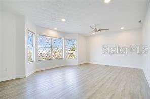 A bright, empty room features light-colored wood-look flooring, a ceiling fan, and large bay windows — 5407 HANSEL AVENUE UNIT G12, ORLANDO, FL