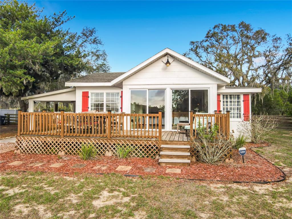 A white house with red shutters features a large wooden deck and sliding glass doors — 1124 SAINT ANNE SHRINE ROAD, LAKE WALES, FL