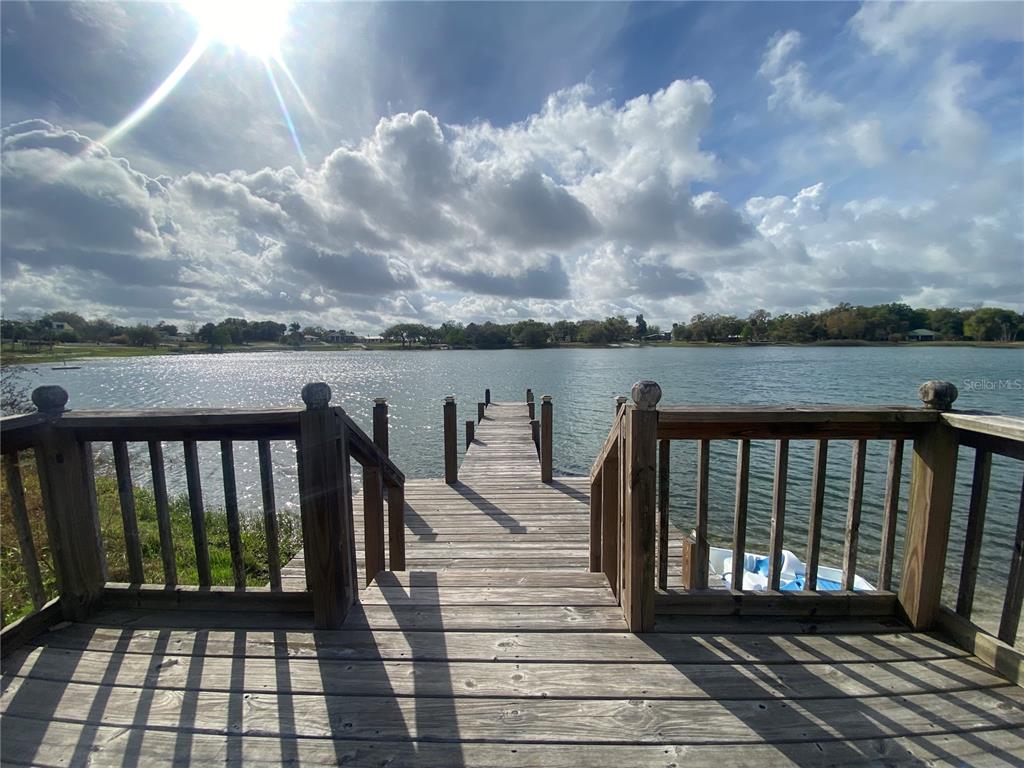 A wooden deck with railings overlooks a lake and a long pier — 1124 SAINT ANNE SHRINE ROAD, LAKE WALES, FL