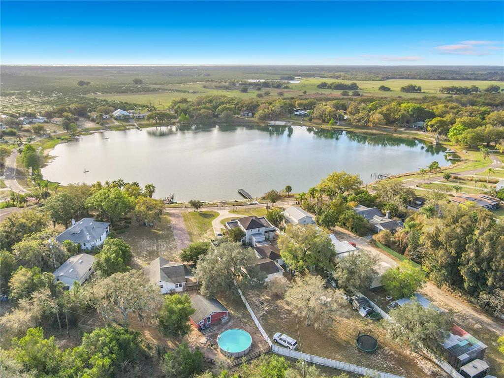 An aerial view shows several houses and a swimming pool situated beside a large lake — 1124 SAINT ANNE SHRINE ROAD, LAKE WALES, FL