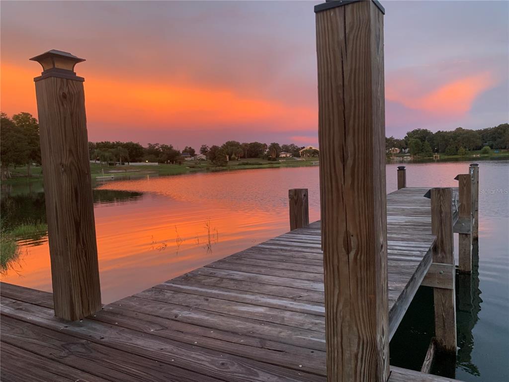 A wooden dock extends into a lake under a vibrant orange and pink sunset sky — 1124 SAINT ANNE SHRINE ROAD, LAKE WALES, FL
