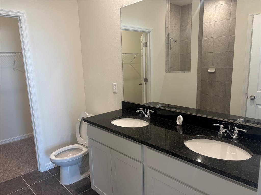 A bathroom features a double vanity with dark granite countertops, light cabinets, and a toilet — 2347 SELENIA STREET, LAKE ALFRED, FL