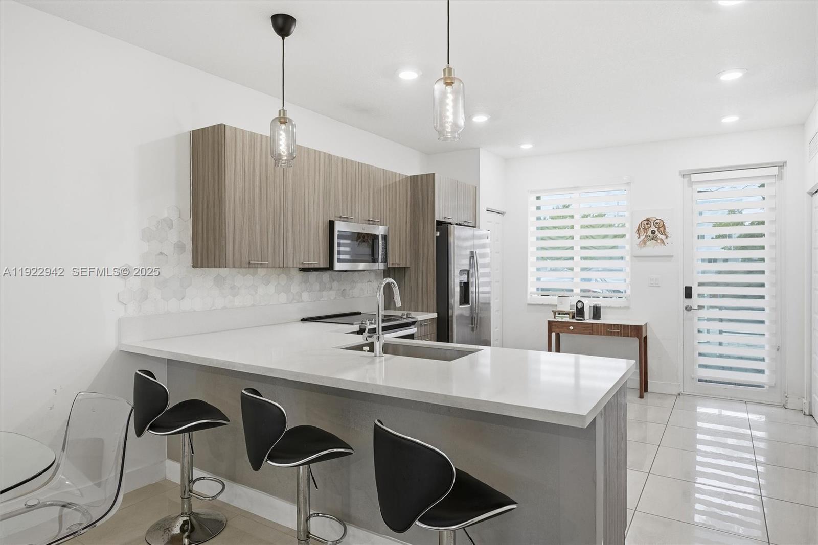 A modern kitchen features a white quartz island, wood-grain cabinets, and three black bar stools — 6420 NW 102nd Path # 110, Doral FL 33178, DORAL, FL