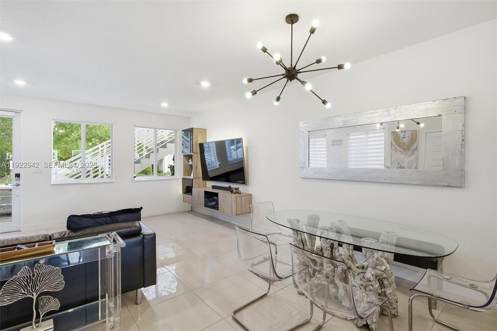 A modern living and dining area features a glass table, chandelier, and wall-mounted television — 6420 NW 102nd Path # 110, Doral FL 33178, DORAL, FL