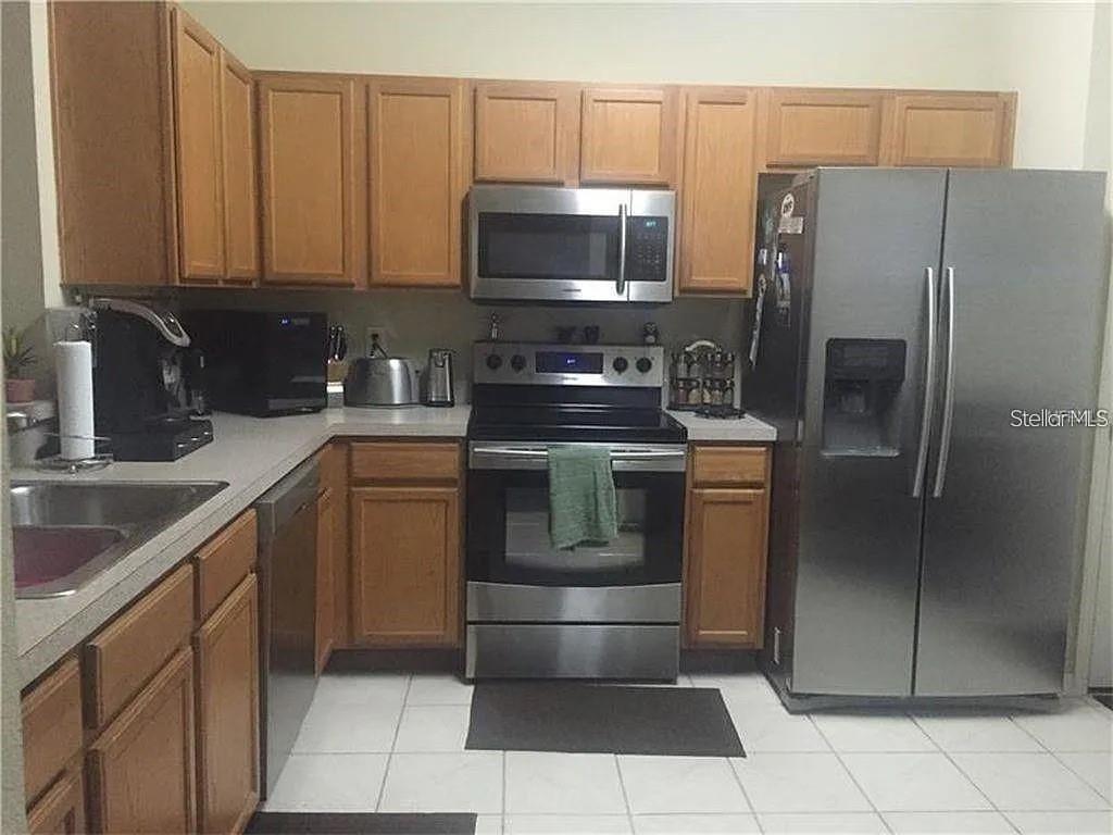A kitchen features wood cabinets, stainless steel appliances, and white tile flooring — 11220 WINDSOR PLACE CIRCLE, TAMPA, FL