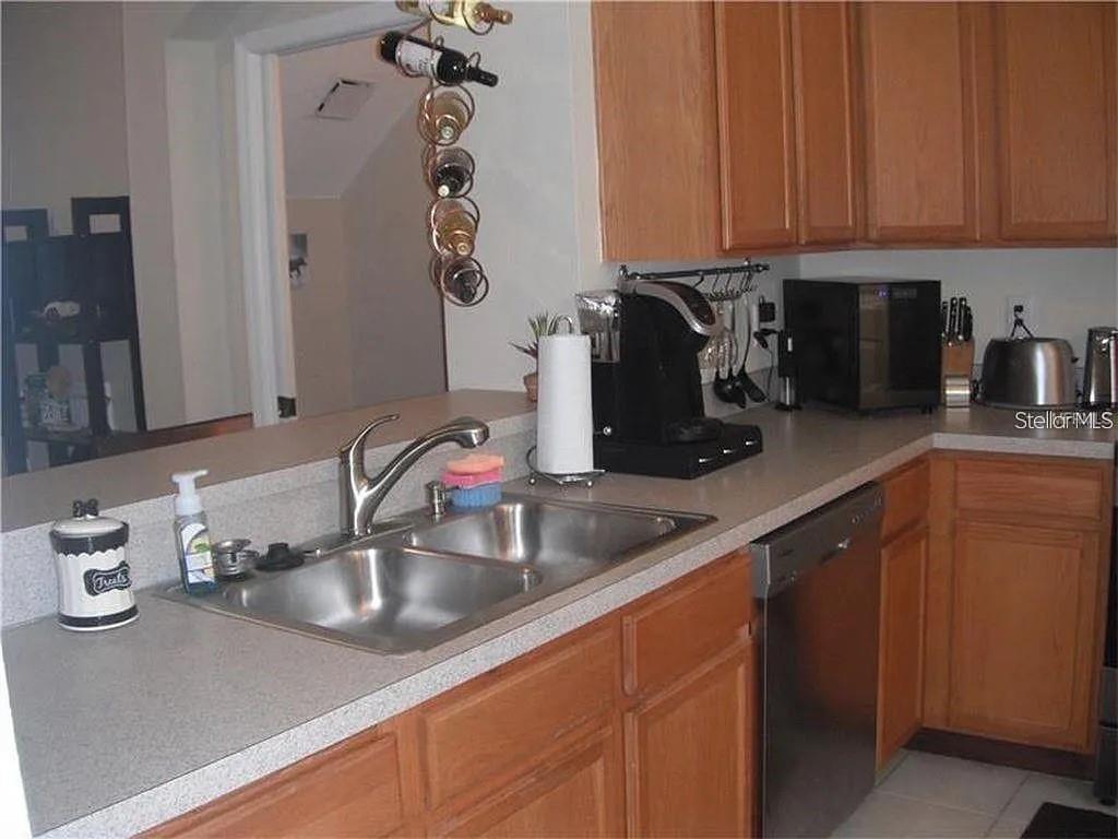 A kitchen features wooden cabinets, a stainless steel sink, and a dishwasher on light countertops — 11220 WINDSOR PLACE CIRCLE, TAMPA, FL