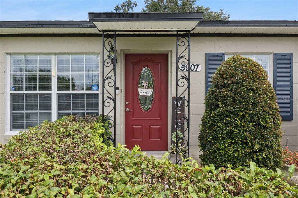 A red front door with an oval window is framed by decorative black metal columns — 5907 DAHLIA DRIVE, ORLANDO, FL