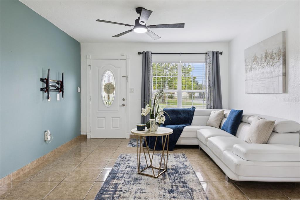 A living room features a white sectional sofa, a blue accent wall, and tiled floors — 5907 DAHLIA DRIVE, ORLANDO, FL