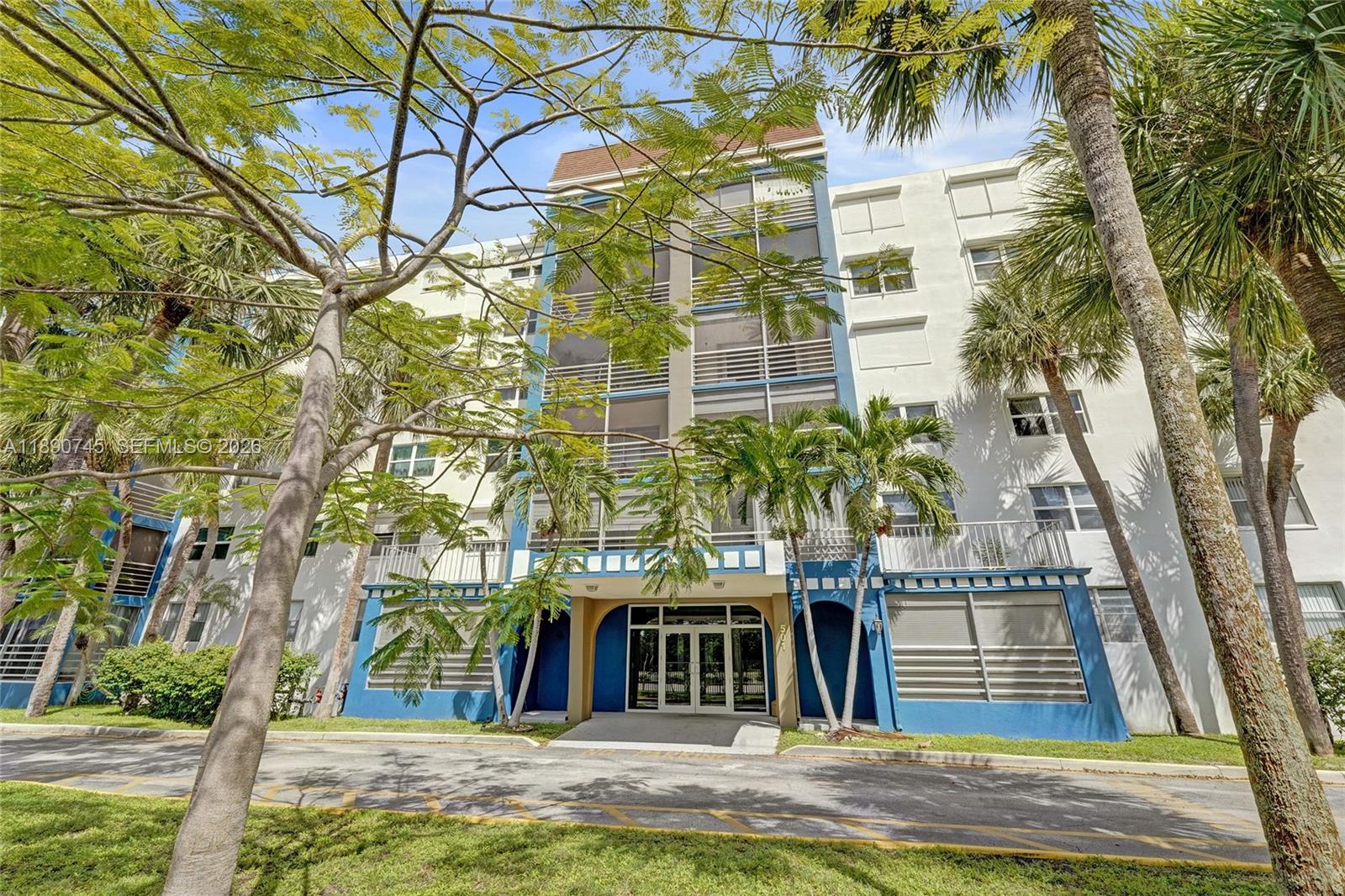 A multi-story residential building features a blue-accented entrance, screened balconies, and surrounding palm trees — 501 E Dania Beach Blvd # 1G, Dania Beach FL 33004, DANIA BEACH, FL