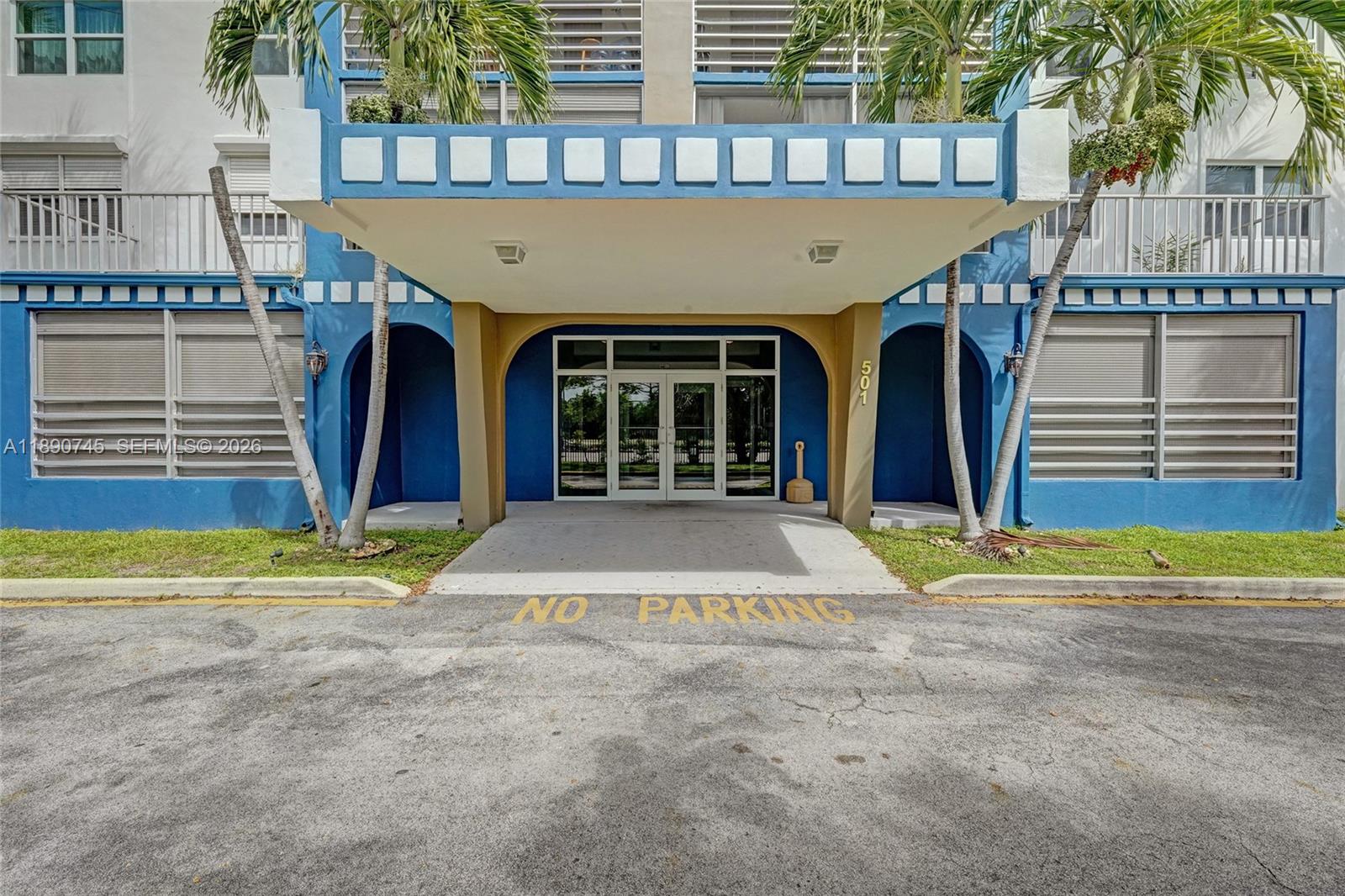 The exterior of a blue building features a covered entrance with glass doors and palm trees — 501 E Dania Beach Blvd # 1G, Dania Beach FL 33004, DANIA BEACH, FL