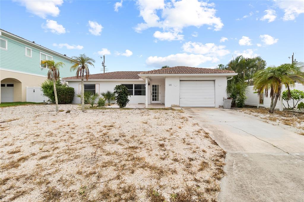 A single-story white house with a tile roof, gravel yard, and attached garage — 158 LIDO DRIVE, ST PETE BEACH, FL