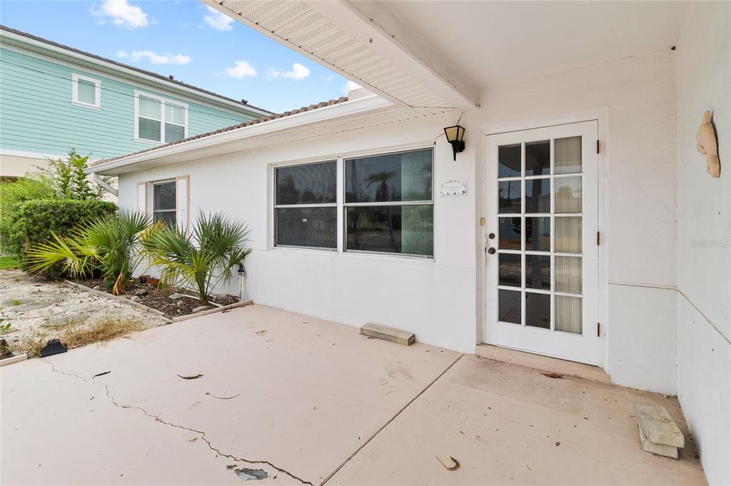 A white exterior wall features a glass-paned door, large windows, and a concrete patio area — 158 LIDO DRIVE, ST PETE BEACH, FL