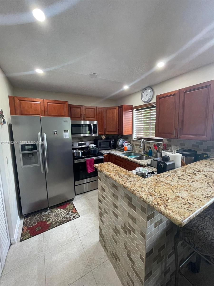 A kitchen features wood cabinets, granite countertops, stainless steel appliances, and a tiled breakfast bar — 13302 SW 152nd St # 3008, Miami FL 33177, MIAMI, FL