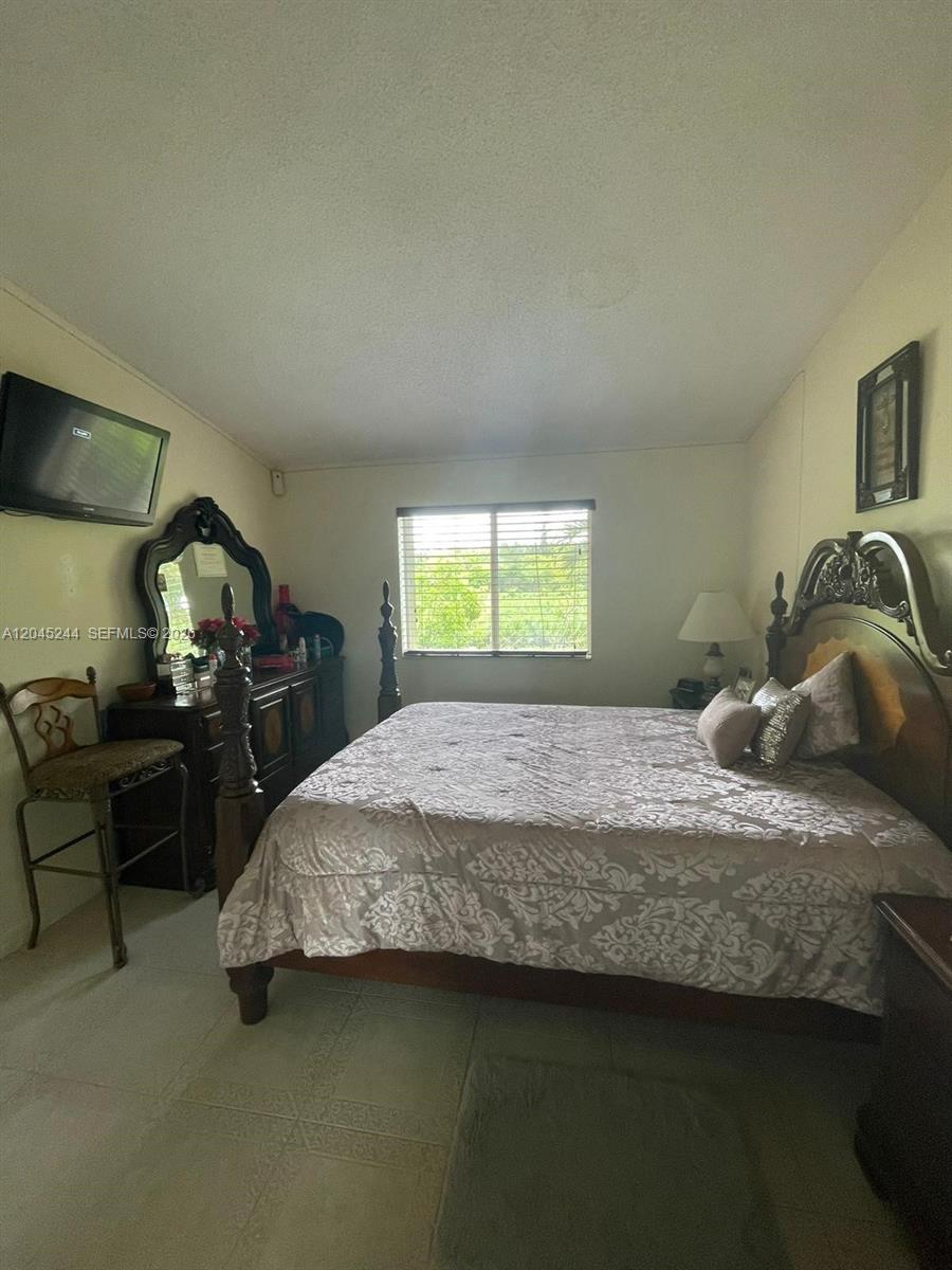 A bedroom features a large wooden bed, a dresser with a mirror, and tiled flooring — 13302 SW 152nd St # 3008, Miami FL 33177, MIAMI, FL