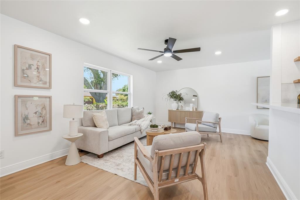 A bright living room features light wood flooring, a neutral sofa, and two wooden armchairs — 5116 18TH AVENUE W, BRADENTON, FL