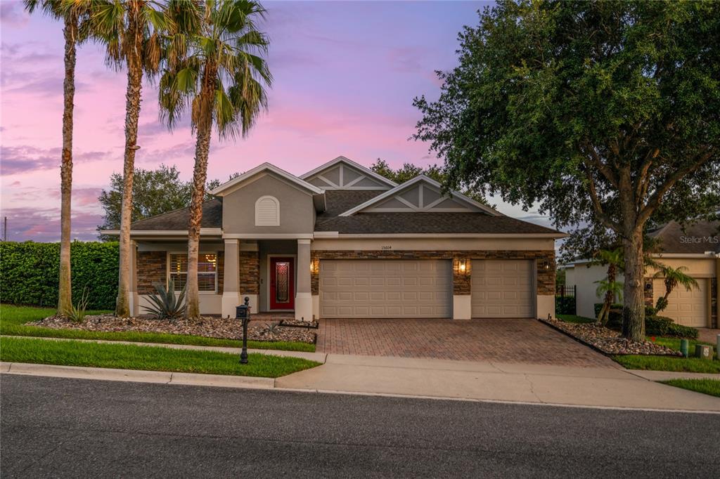 A single-story house with a stone facade, two-car garage, and palm trees at dusk — 15604 GRANLUND STREET, WINTER GARDEN, FL