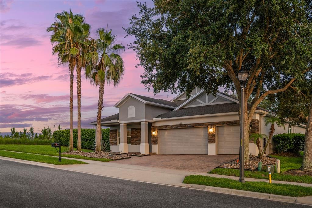 A single-story house with a two-car garage, stone accents, and palm trees under a sunset sky — 15604 GRANLUND STREET, WINTER GARDEN, FL