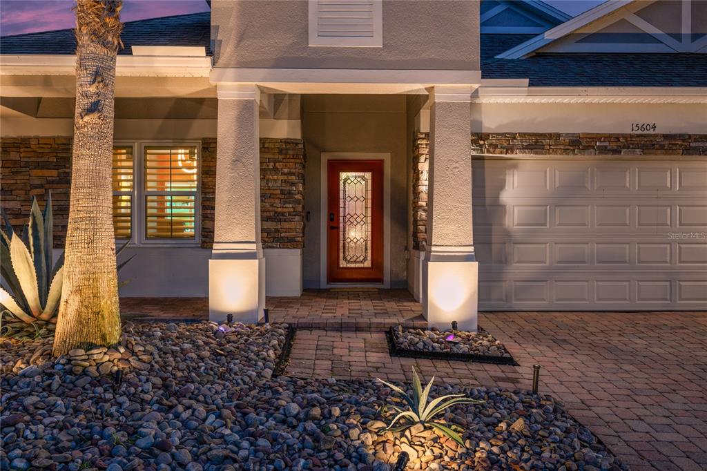 The exterior of a house features a stone facade, a red front door, and landscaping — 15604 GRANLUND STREET, WINTER GARDEN, FL