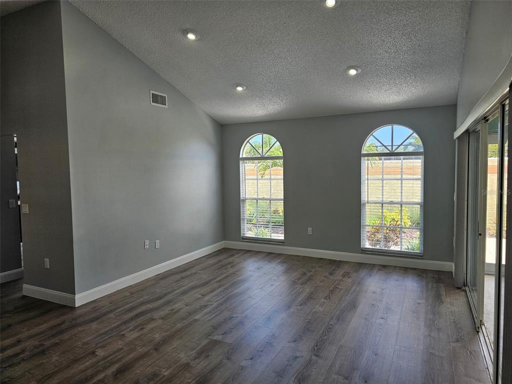 An empty room with gray walls, wood-look flooring, vaulted ceilings, and two arched windows — 3625 57TH AVENUE DRIVE W, BRADENTON, FL