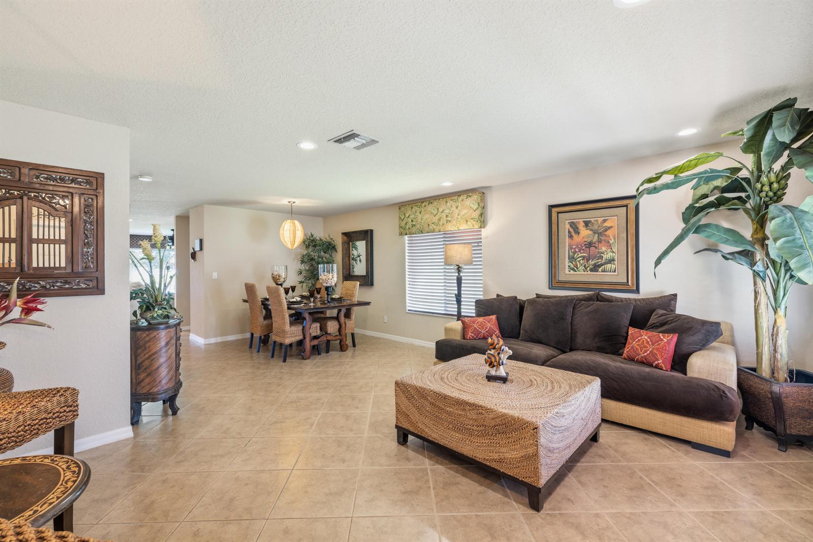 A living room and dining area with tile floors, a brown sofa, and tropical decor — 5580 45th Avenue, Vero Beach FL 32967, VERO BEACH, FL