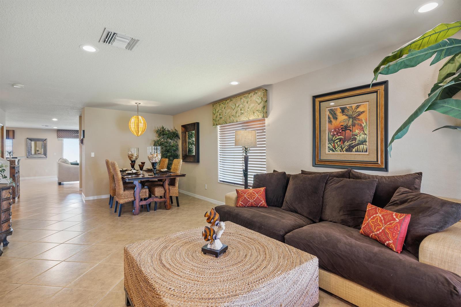 A living room with a brown sofa and woven ottoman flows into a dining area — 5580 45th Avenue, Vero Beach FL 32967, VERO BEACH, FL