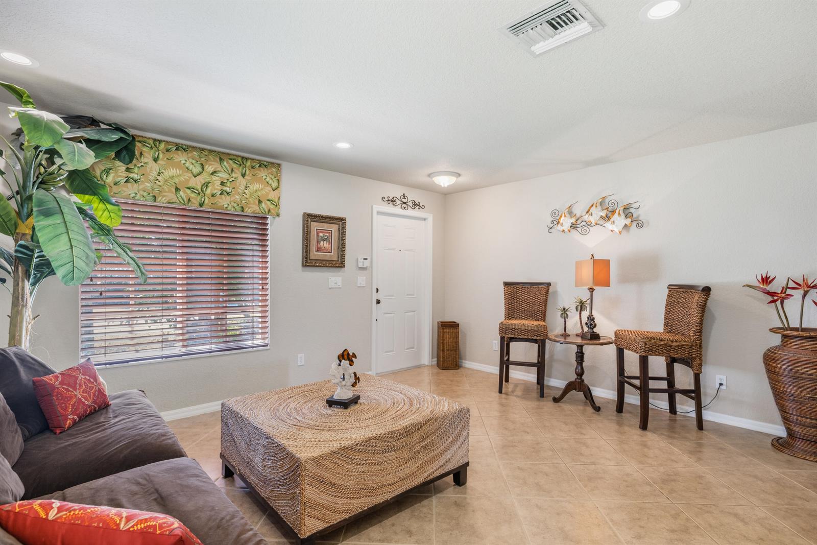 A living room features tile floors, a woven coffee table, two bar stools, and a sofa — 5580 45th Avenue, Vero Beach FL 32967, VERO BEACH, FL