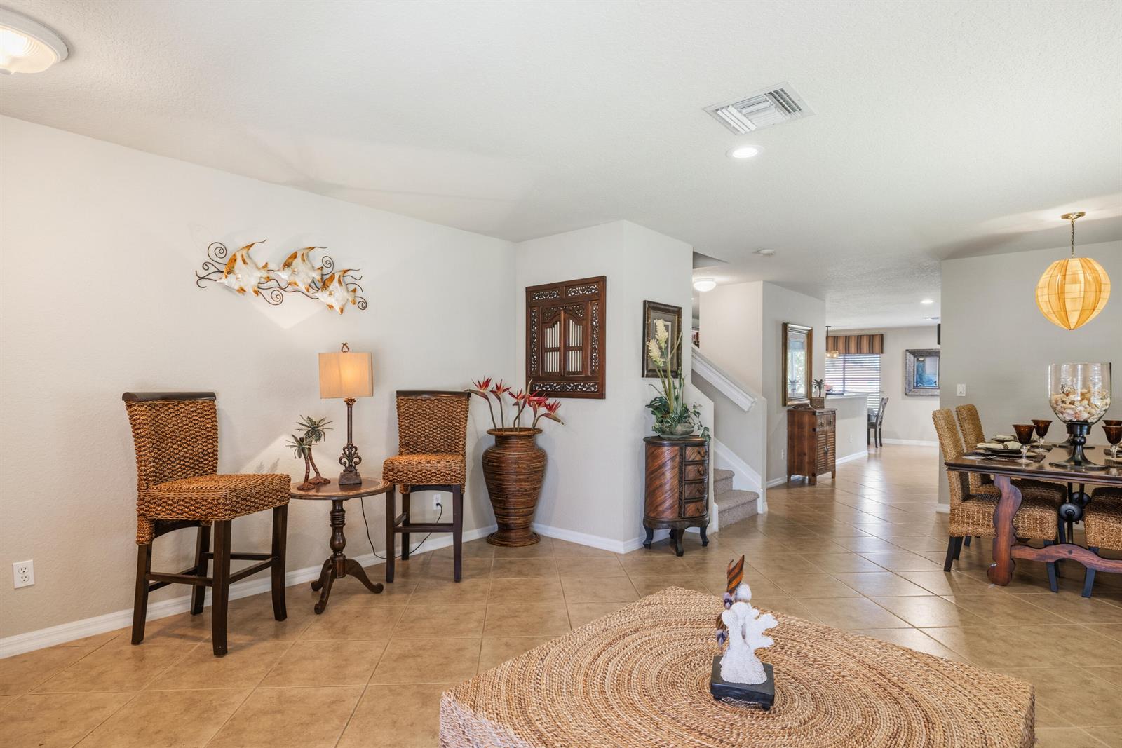 A dining area and living space feature tile flooring, woven furniture, and neutral walls — 5580 45th Avenue, Vero Beach FL 32967, VERO BEACH, FL