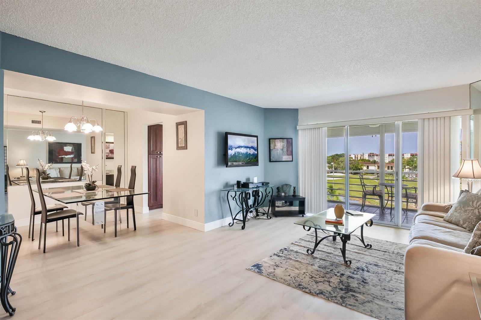 A living and dining area features light wood flooring, blue accent walls, and a balcony view — 3593 Birdie Drive # 507, FL 33467, FL