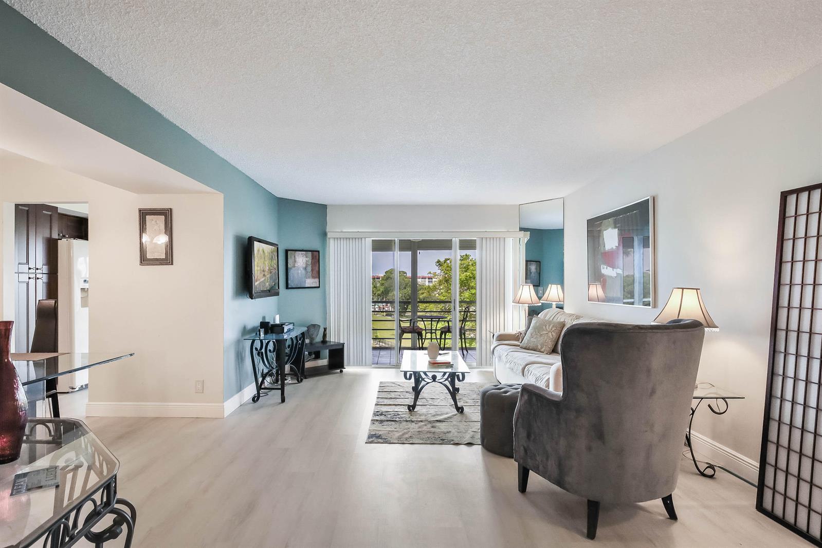 A living room features light wood-look flooring, a blue accent wall, and a sliding glass door — 3593 Birdie Drive # 507, FL 33467, FL