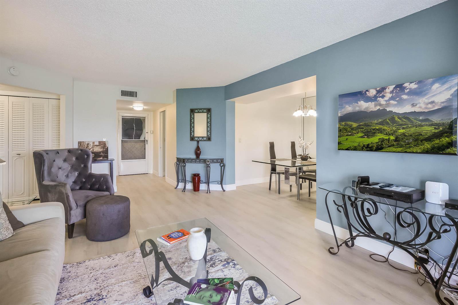 A living room with light wood flooring, a grey armchair, and a wall-mounted television — 3593 Birdie Drive # 507, FL 33467, FL