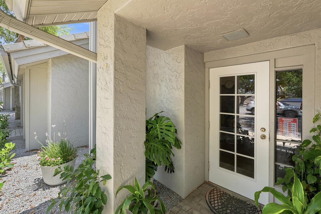 A white front door with glass panes sits under a covered entryway with potted plants — 1515 TAMIAMI TRAIL S UNIT 2A, VENICE, FL