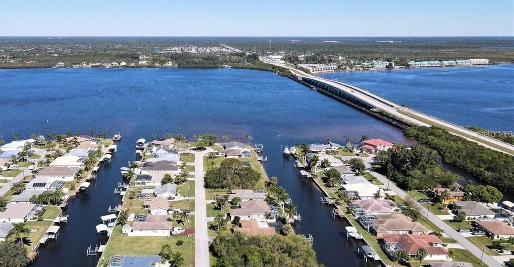 An aerial view shows waterfront houses along canals leading to a large bay and bridge — 12739 BACCHUS ROAD, PORT CHARLOTTE, FL