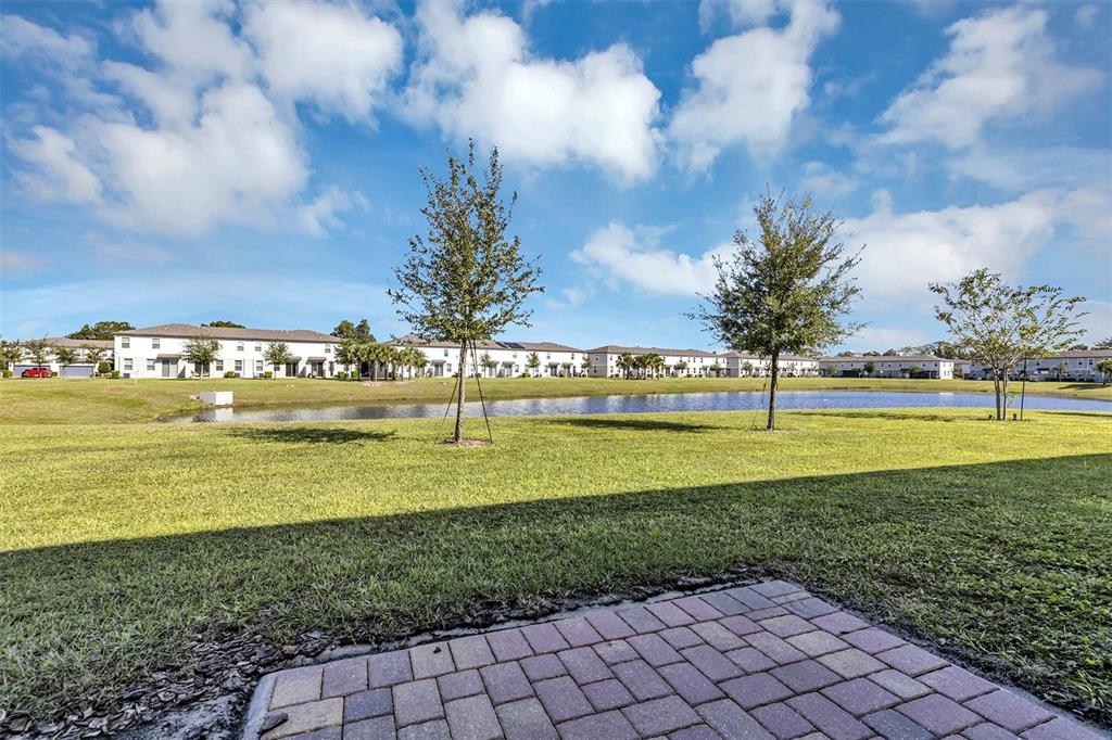 A view of a grassy lawn, a small pond, and residential buildings under a blue sky — 1073 DESERT CANDLE DRIVE, OCOEE, FL