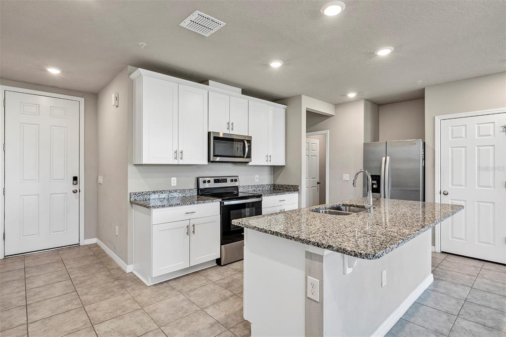 A kitchen features white cabinets, granite countertops, stainless steel appliances, and a central island — 1073 DESERT CANDLE DRIVE, OCOEE, FL