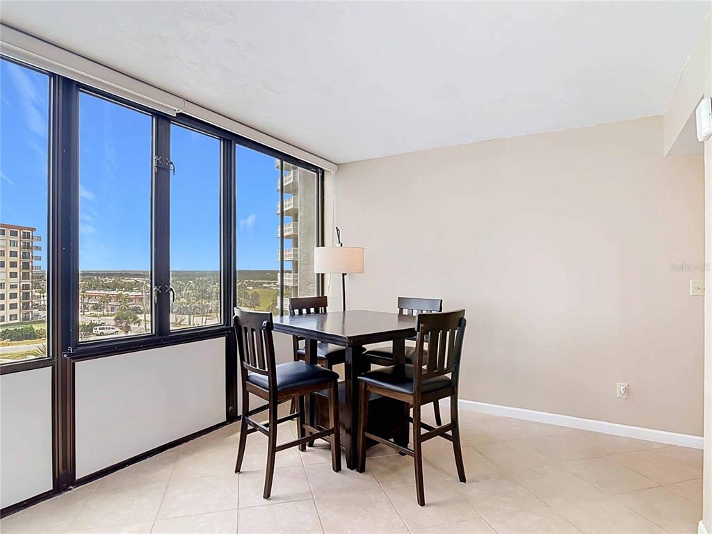 A dining area features a dark wood table and chairs beside floor-to-ceiling windows — 3580 S OCEAN SHORE BOULEVARD UNIT 506, FLAGLER BEACH, FL