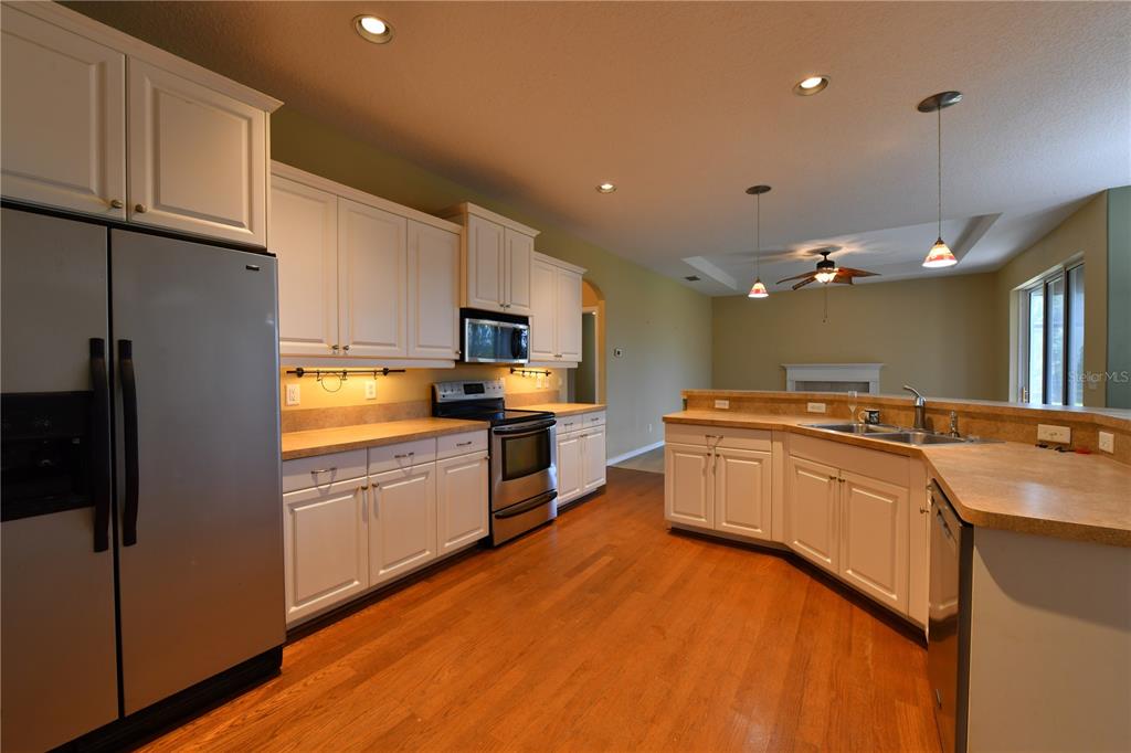 A kitchen with white cabinets, stainless steel appliances, and wood flooring opens to a living area — 2509 155TH AVENUE E, PARRISH, FL