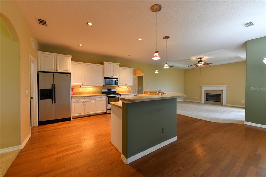 A kitchen with white cabinets and stainless steel appliances overlooks a carpeted living area — 2509 155TH AVENUE E, PARRISH, FL