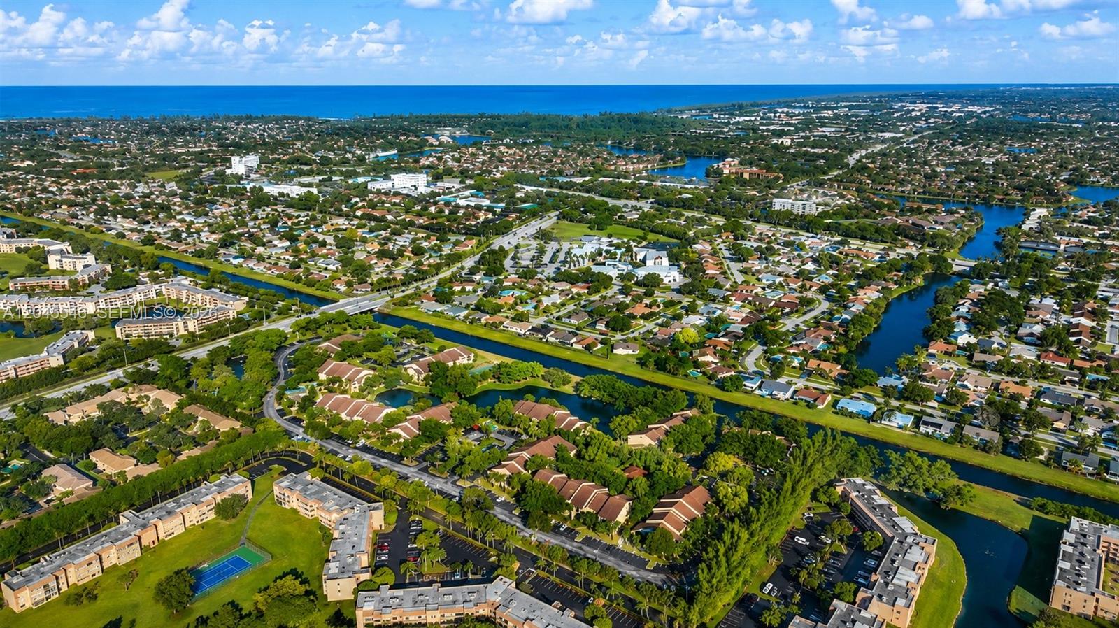 An aerial view shows a residential neighborhood with apartment complexes, canals, and green spaces — 9999 Summerbreeze Dr # 317, Sunrise FL 33322, SUNRISE, FL