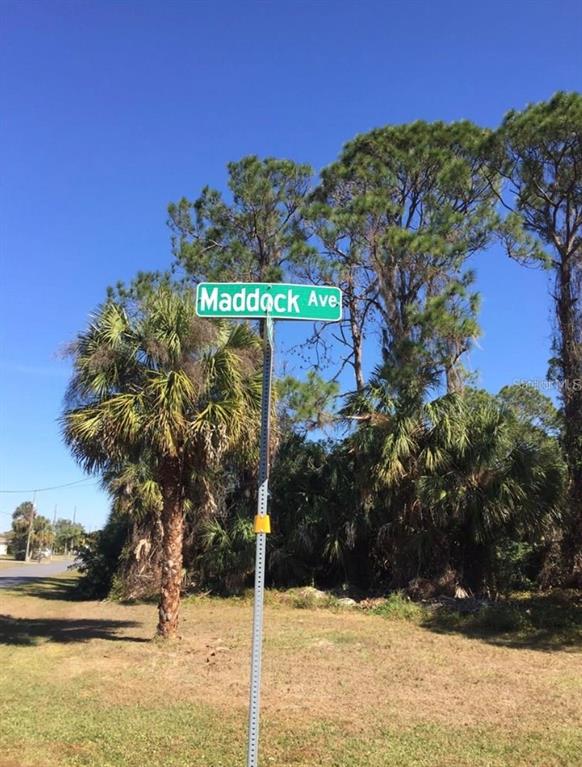 A green street sign reading Maddock Ave stands on a metal pole near palm trees — 14423 MADDOCK AVENUE, PORT CHARLOTTE, FL