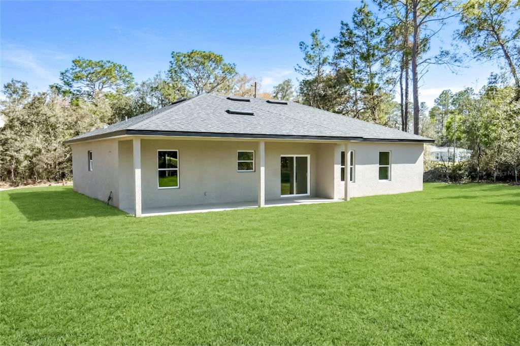 The rear exterior of a single-story house with a covered patio and a large lawn — 7872 N KEYSTONE DRIVE, CITRUS SPRINGS, FL