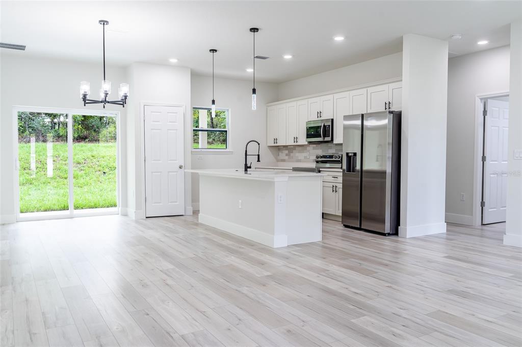 A modern kitchen features white cabinetry, stainless steel appliances, a center island, and wood-look flooring — 7872 N KEYSTONE DRIVE, CITRUS SPRINGS, FL