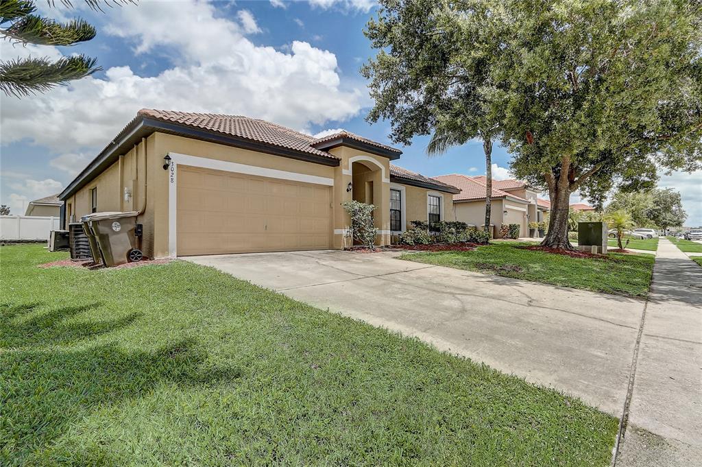 A single-story tan stucco house with a two-car garage and a concrete driveway — 3028 CAMINO REAL DRIVE S, KISSIMMEE, FL