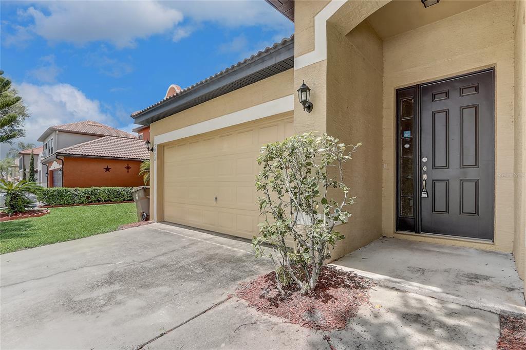 A beige house exterior features a two-car garage, a dark front door, and landscaping — 3028 CAMINO REAL DRIVE S, KISSIMMEE, FL