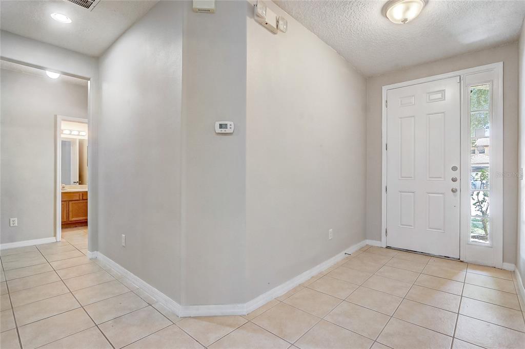 A tiled entryway features a white front door with a sidelight and a wall-mounted thermostat — 3028 CAMINO REAL DRIVE S, KISSIMMEE, FL