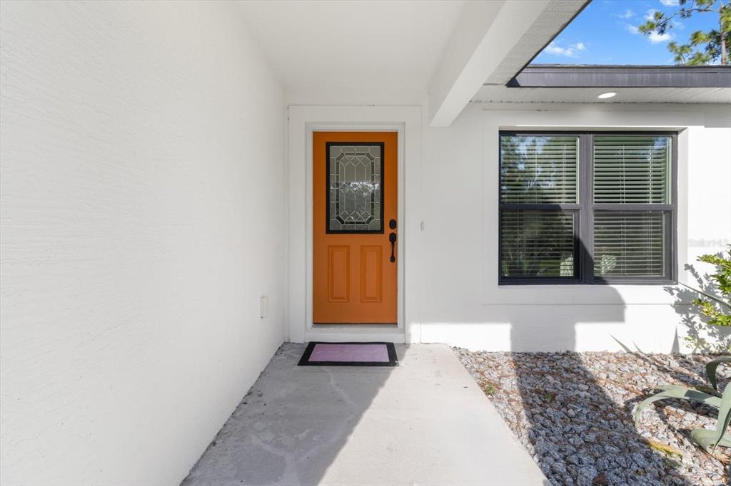 An exterior view of a home entrance with a bright orange door and white walls — 11855 W FLAXEN DRIVE, CRYSTAL RIVER, FL