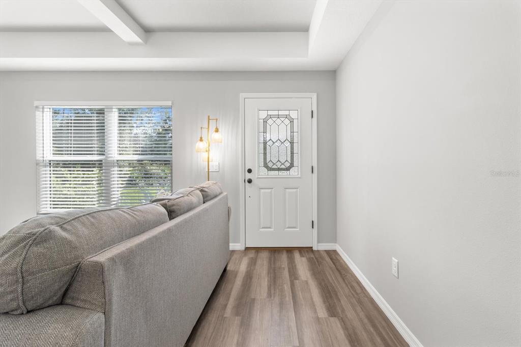 A living room features a grey sofa, wood-look flooring, a white front door, and windows — 11855 W FLAXEN DRIVE, CRYSTAL RIVER, FL