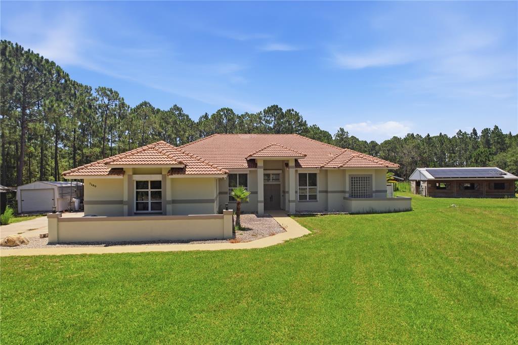 A single-story house with a tiled roof, beige stucco exterior, and a large grassy yard — 7190 SIX GUN COURT, ST CLOUD, FL